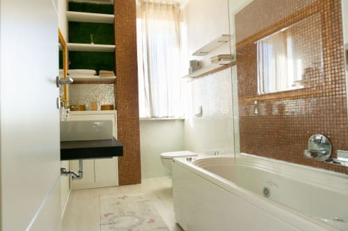 Luxury bathroom at Versilia Panoramic in Como with brown mosaic tiles, white bathtub, and built-in sink vanity