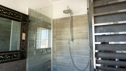 Modern luxury bathroom shower with glass enclosure, rainfall showerhead, and wood-tone tile walls at Versilia Panoramic