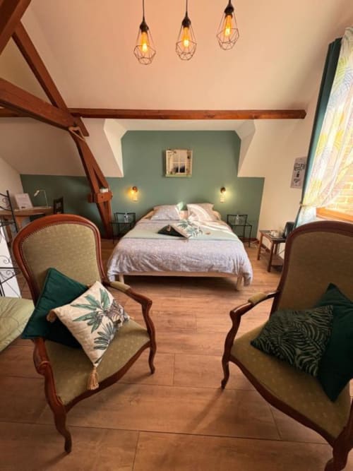Chambre Verveine à la Ferme de la Forterie : élégante chambre avec mur d'accent vert, poutres en bois, mobilier d'époque et jardin
