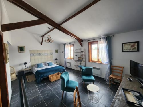 Spacious bedroom at Ferme de la Forterie with exposed beams, blue bedding, teal armchair, and garden views through windows
