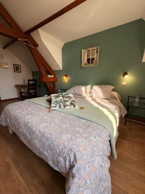Chambre mansardée douillette aux murs vert sauge, poutres apparentes, lit confortable avec parure motifs, à la Ferme de la Forterie