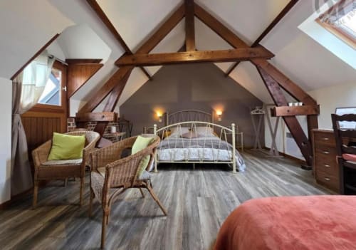 Spacious loft bedroom at Ferme de la Forterie with exposed beams, metal bed, wicker chairs, and garden view