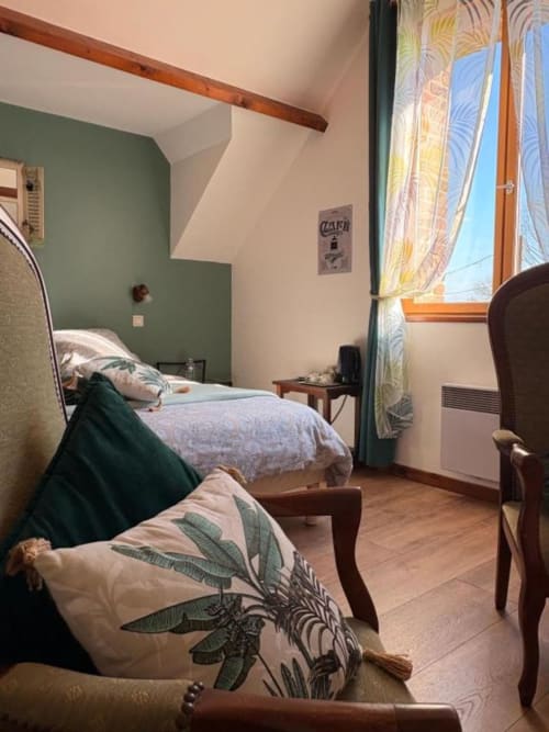 Chambre douillette à la Ferme de la Forterie avec mur accent vert, poutres en bois, fenêtres vue jardin et décor traditionnel