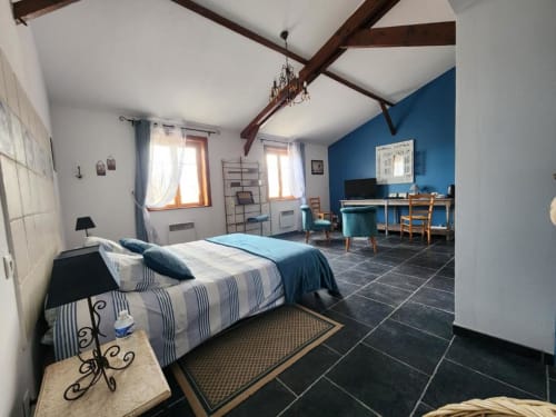 Spacious bedroom at Ferme de la Forterie with blue accent wall, exposed beams, striped bedding, and work desk area with