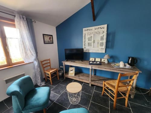 Modern hotel room with blue accent wall, wooden desk, TV, teal armchair, and fireplace at Ferme de la Forterie in Verlinghem