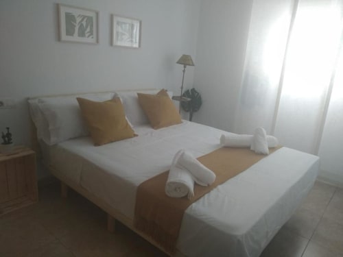 Bright modern bedroom at Love Rent4 Malaga with white bed, gold pillows, rolled towels, lamp, and city views in Torremolinos