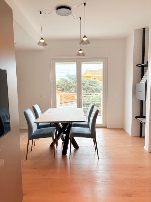 Elegante zona living nell'appartamento Le Dimore di Giò a Ortona: pavimenti in legno, tavolo moderno, sedie grigie e lampadari a sospensione