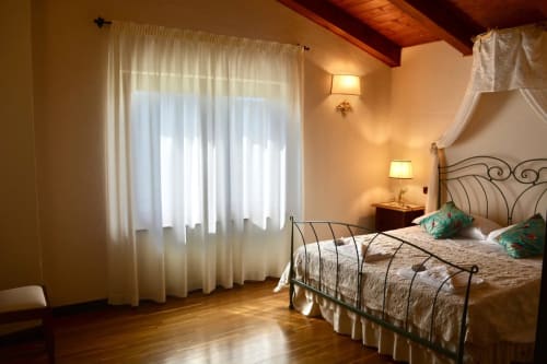 Elegant bedroom at Agriturismo Colle Mura in Gualdo Tadino with wrought iron bed, sheer curtains, and warm lighting