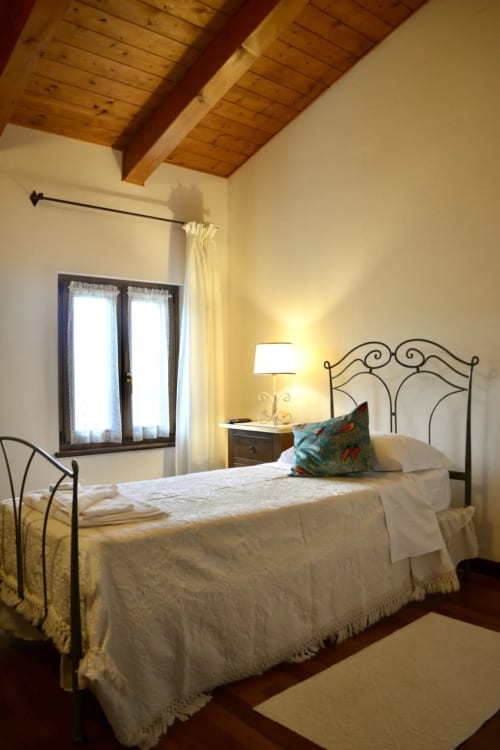 Bright bedroom at Agriturismo Colle Mura with wrought iron bed, wooden ceiling beams, and natural light from windows