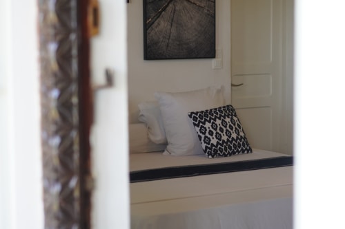 Chambre double confortable à Kaz Kafe à Mamoudzou avec oreillers blancs et coussin à motifs sur le lit, tableau vue jardin au-dessus, ouverte