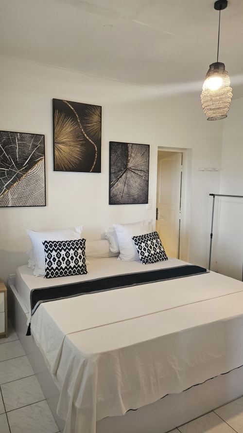 Modern double bedroom at Kaz Kafe Mamoudzou with white bedding, black geometric pillows, pendant lamp, and abstract wall art.