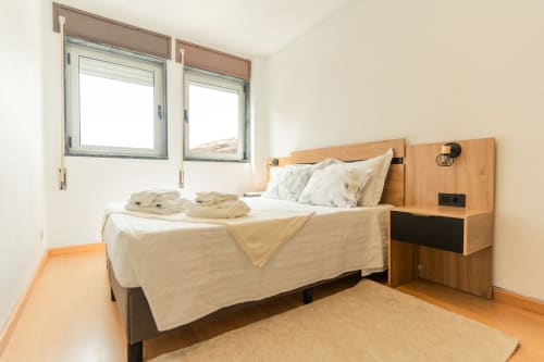 Quarto moderno do apartamento DouroParadise em Fontelas com cama de madeira, roupa de cama bege, janelas duplas e vista para o rio