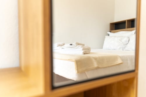 Reflexo no espelho do quarto do apartamento DouroParadise com almofadas brancas, toalhas bem dobradas e roupas de cama bege em Fontelas,