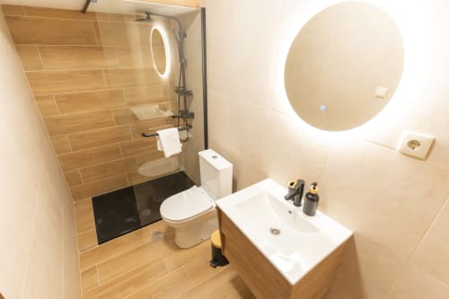 Banheiro moderno com revestimento tipo madeira, chuveiro espaçoso, WC, pia e espelho iluminado redondo no DouroParadise