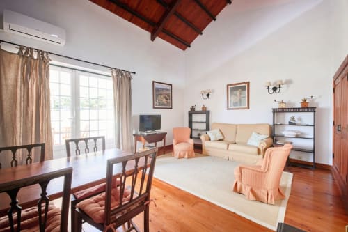 Sala de estar da Casa do Lagar na Quinta da Alcaidaria-Mór com sofá creme, mesa de jantar e vista para o jardim