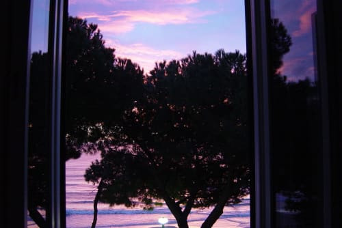 Sonnenuntergangsblick vom Balkon des Hotel Beau Rivage in Alassio, Italien, mit silhouettierten Palmen, die das ruhige Meer rahmen