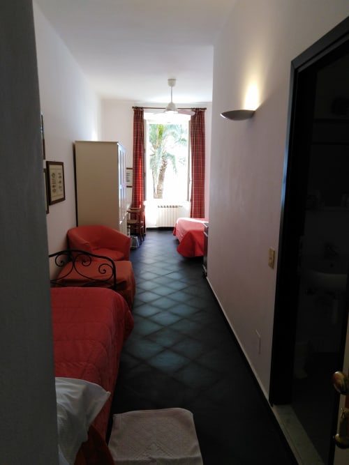 Spacieuse chambre triple à l'Hôtel Beau Rivage d'Alassio avec lits à couverture rouge, carrelage foncé et vue sur mer par la façade