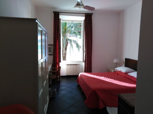 Helles Schlafzimmer im Hotel Beau Rivage Alassio mit roter Bettwäsche, Meerblick durch die Balkontür und Deckenventilator