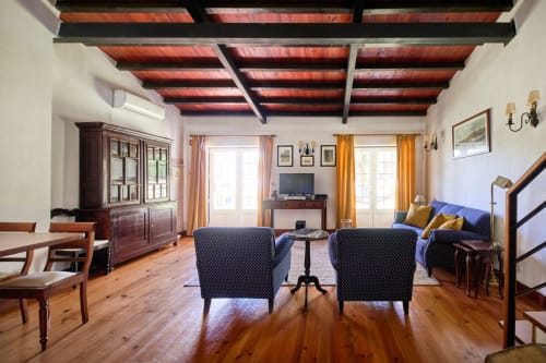 Espaçosa sala de estar da villa Quinta da Alcaidaria-Mór com vigas de madeira, poltronas azuis e vista para o jardim em Fátima,