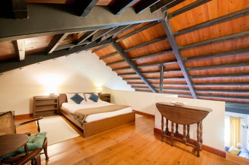 Espaçoso quarto no sótão da Quinta da Alcaidaria-Mór com vigas de madeira, cama de casal, mesa de jantar e teto em madeira aparente