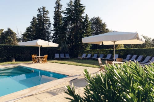Área de piscina da Quinta da Alcaidaria-Mór em Ourém com espreguiçadeiras, guarda-sóis e paisagem de árvores coníferas