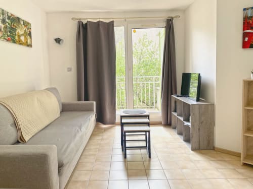 Séjour lumineux au Vallon des Sources avec canapé beige, téléviseur, balcon avec vue montagne et carrelage terre cuite