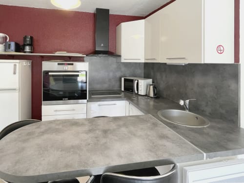 Cuisine moderne aux armoires blanches, comptoirs foncés et murs bordeaux de l'Appartement 103 au Vallon des Sources