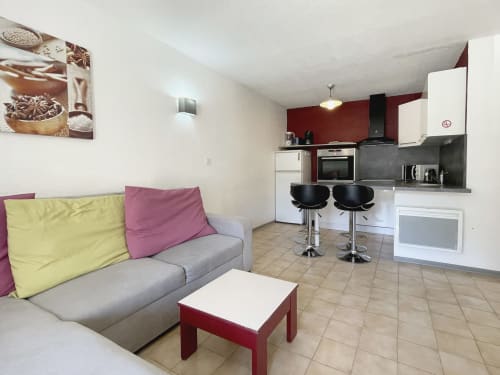 Studio moderne au Vallon des Sources avec canapé gris, cuisine équipée et accents rouges à Digne-les-Bains