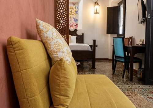 Habitación de lujo en Villa Merida con sillón amarillo, paredes rosa y muebles de madera oscura en Mérida, México