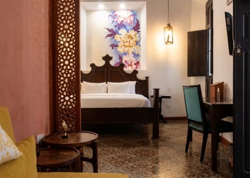 Habitación del Villa Merida Boutique Hotel con cama de madera ornamentada, asientos amarillos, arte floral y decoración tradicional de Mérida