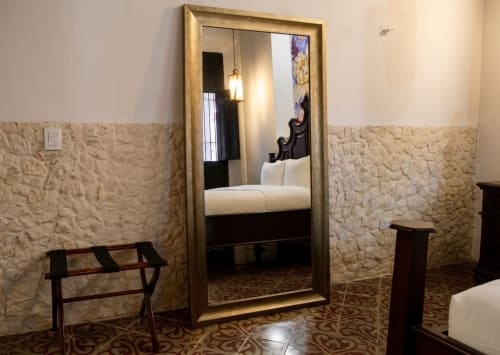 Dormitorio elegante en Villa Merida Boutique Hotel con paredes de piedra, espejo de cuerpo entero y muebles de madera oscura