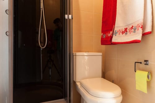 Banheiro moderno com box de chuveiro em vidro, vaso sanitário branco e toalhas decorativas vermelha e creme em Casa da Lagiela, B&B rural