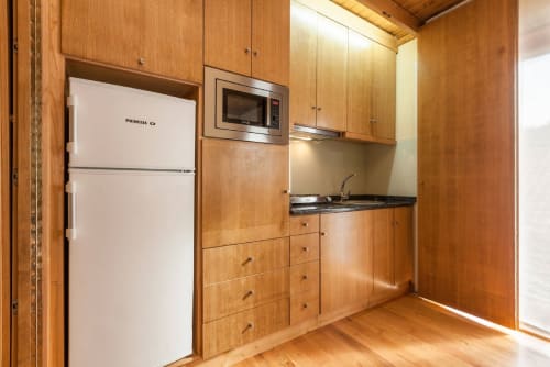 Cozinha de estúdio com painéis de madeira na Casa da Lagiela, Fafe, com geladeira branca, micro-ondas, fogão e área de refeições