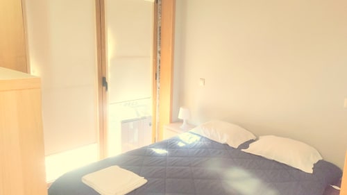 Quarto iluminado com cama de casal, almofadas brancas, colcha azul-marinho, porta de madeira e vista para a piscina na Casa da Lagiela em Fafe