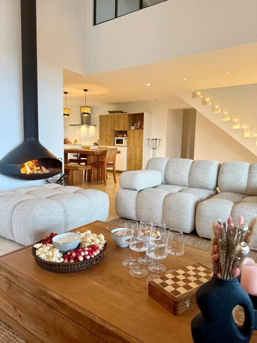 Salon moderne de la Villa Le Cap à Sainte-Maxime : canapé crème courbé, cheminée, salle à manger boisée et escalier