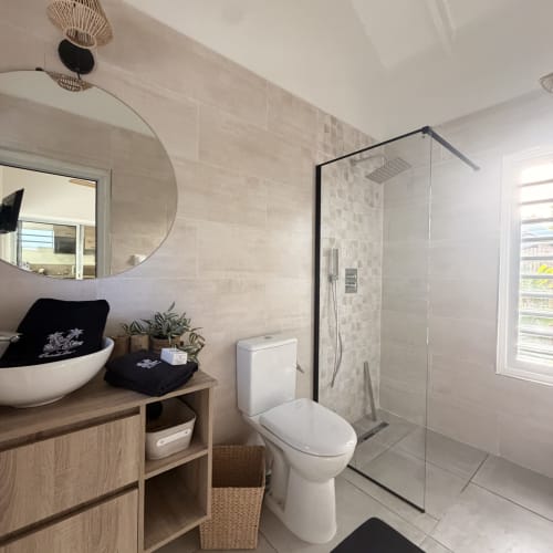 Modern bathroom at Filao Cottage with white vessel sink, glass shower enclosure, toilet, and beige tile walls in Sainte-Rose,