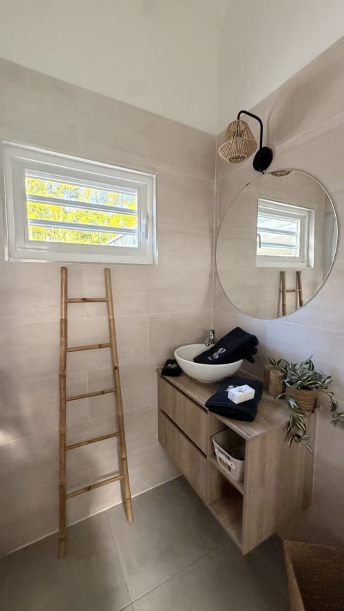 Modern bathroom at Filao Cottage in Sainte-Rose with round mirror, vessel sink, wooden ladder, potted plant, and natural