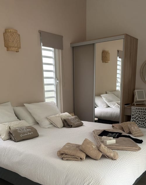 Modern cottage bedroom at Filao Cottage in Sainte-Rose with white bedding, mirrored wardrobe, woven pendant lights, and