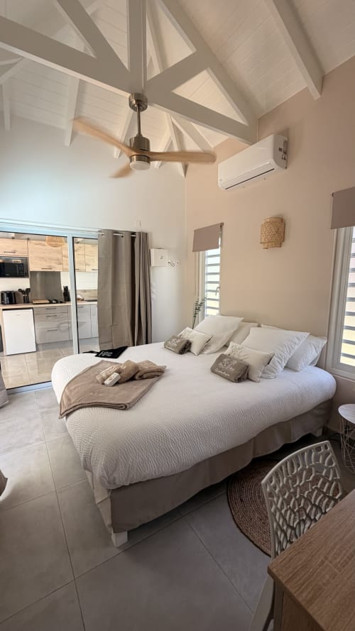 Bright bedroom at Filao Cottage in Sainte-Rose with queen bed, ceiling fan, kitchenette, and high vaulted ceilings