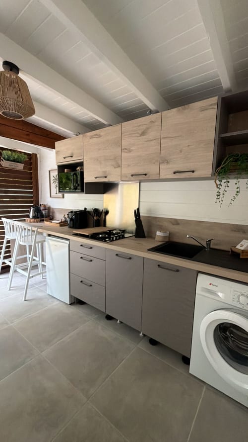 Modern kitchen in Filao Cottage with light wood cabinets, black countertop, gas stove, sink, washing machine, and white