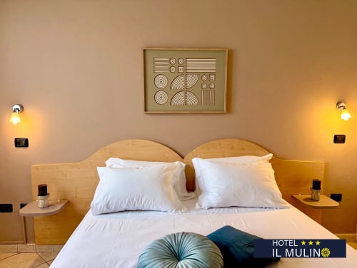 Camera doppia standard dell'Hotel Il Mulino a Villalunga con biancheria bianca, testiere in legno e arte geometrica alle pareti
