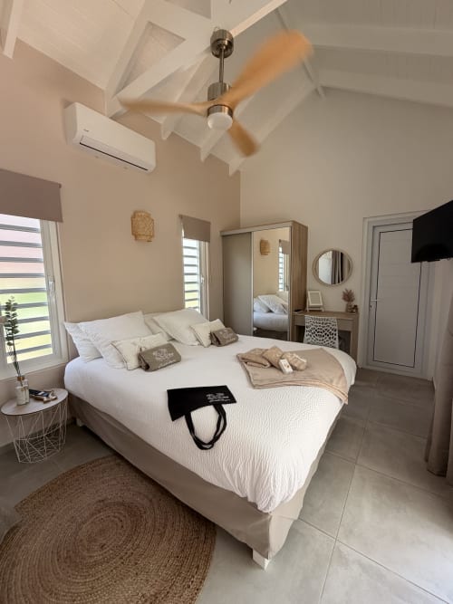 Bright cottage bedroom at Filao in Sainte-Rose with white bed, ceiling fan, AC unit, and modern décor