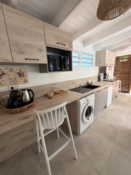 Modern kitchen in Filao Cottage, Sainte-Rose with wood cabinetry, white bar stool, and stainless appliances