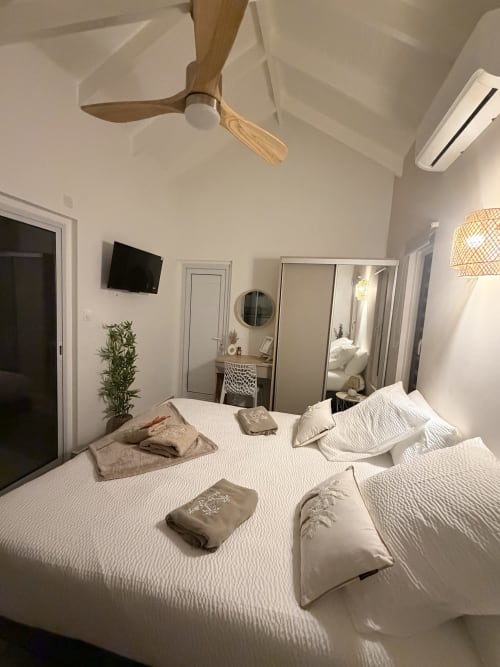 Modern bedroom at Filao Cottage BnB in Sainte-Rose with white bedding, wooden ceiling fan, and mirror
