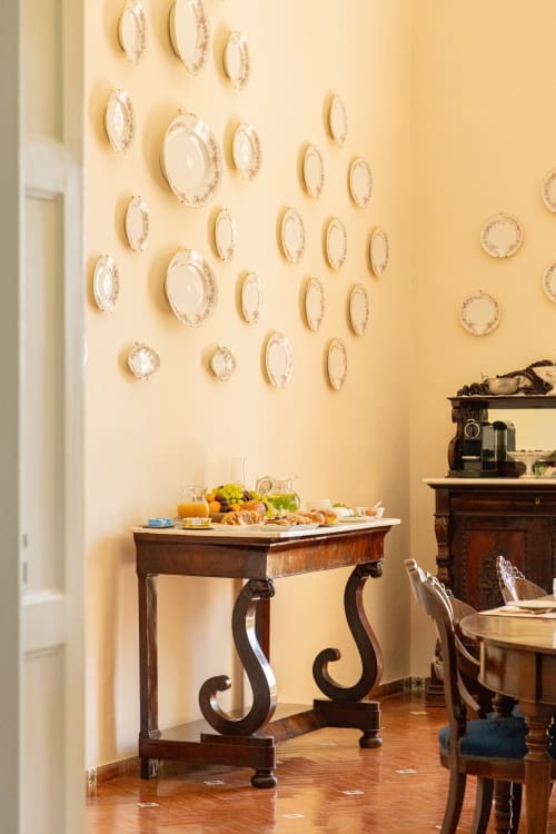 Elegante sala da pranzo di Villa Ceci B&B ad Andria con piatti decorativi su parete gialla e antico tavolo in legno