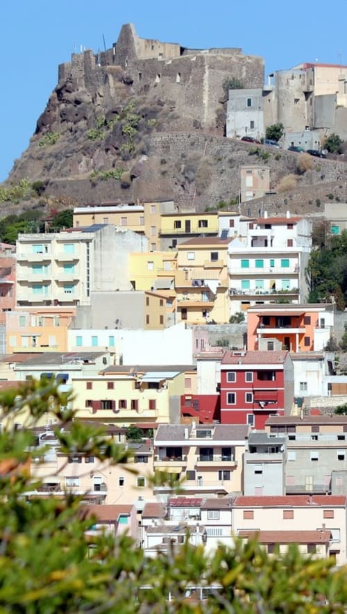 Edifici colorati arroccati su una collina con i resti di un antico castello a Valledoria, Italia