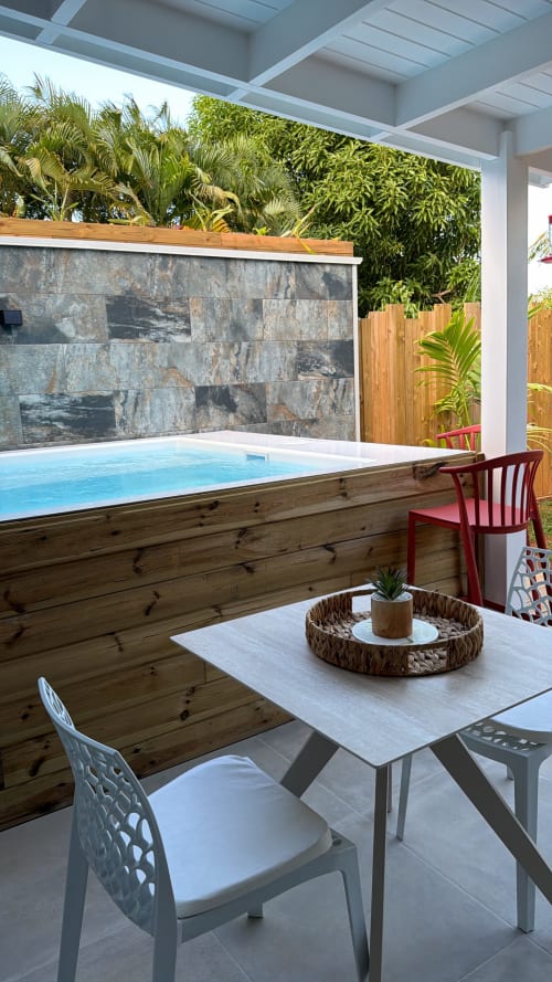 Modern pool area at Filao Cottage with wooden deck, stone water feature, dining table, and tropical garden in Guadeloupe