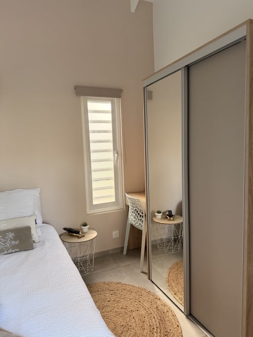 Modern bedroom at Filao Cottage with mirrored wardrobe, white bed, woven rugs, and louvered window in Sainte-Rose