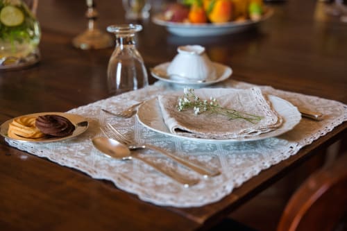 Elegante tavolo presso Villa Ceci Andria con tovaglietta in pizzo, piatto bianco, fiori freschi e pasticcini gourmet