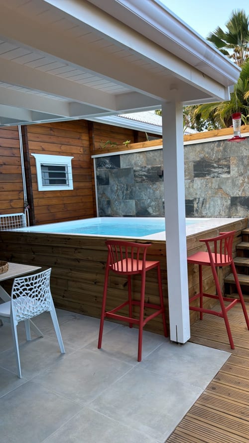 Filao Cottage outdoor bar with blue pool, red stools, stone wall, wooden deck and palm trees in Sainte-Rose, Guadeloupe